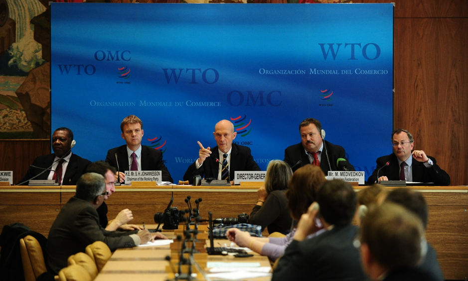 Men on podium and delegates at WTO conference. Photo.