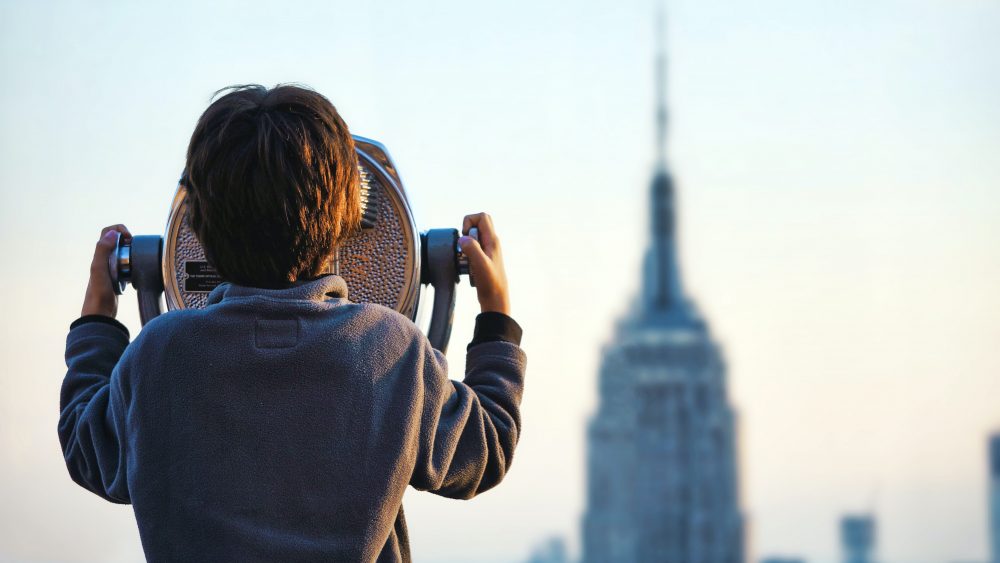 Child looking at high building with binoculars. Photo.
